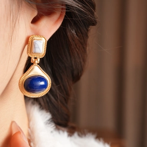 Detail of vintage matte gold earrings with blue drop gemstone worn by model in soft light