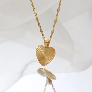 Golden heart pendant necklace with sunburst texture on white fabric background