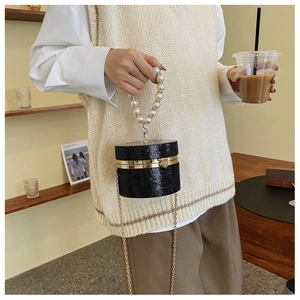 Detail of a sparkling black rhinestone cylinder bag with pearl handle and golden chain