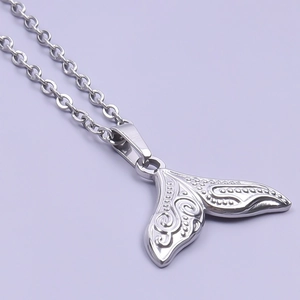 Detailed close-up of a silver stainless steel whale tail pendant with engraved patterns