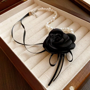 Close-up of pearl necklace with a black fabric rose in a beige suede jewelry box