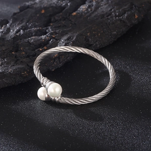 Detailed close-up of a silver twisted cable cuff bracelet featuring two white faux pearls