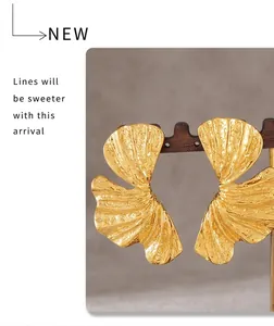 Macro detail of golden ginkgo leaf earrings with textured hammered finish on wood stand