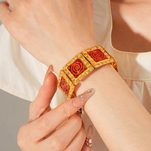 Detail of vintage gold bracelet featuring red enamel square charms with spiral patterns