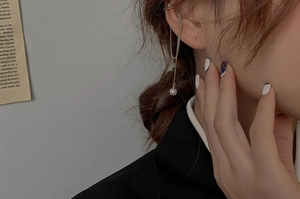 Detail shot of a silver metal ear cuff with a long chain and white pearl on a model