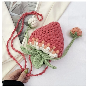 Detail of pink hand-knitted strawberry bucket bag with green leaves and berry charms