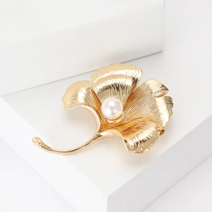 Elegant gold ginkgo leaf brooch featuring a white pearl on a clean minimalist background