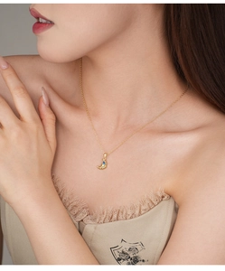 Detailed view of a gold croissant pendant necklace with a blue gemstone on a model