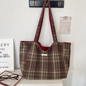 Detail of a brown plaid tote bag with red lining and a woven label on a white wall
