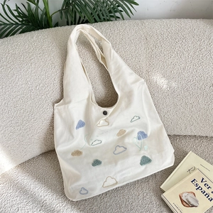 Detail of embroidered colorful clouds on beige canvas tote bag with magnetic snap