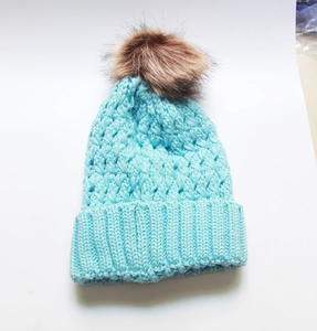 Detail of light blue cable knit beanie with brown faux fur pom pom on white background