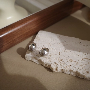 Macro shot of minimalist silver bean studs on white stone with elegant metal luster