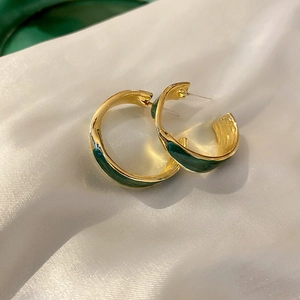 Macro shot of gold-plated irregular C-shape earrings with green enamel on silk