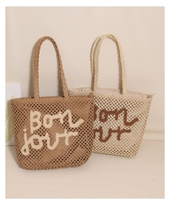 Detail of hand-woven straw tote bags with embroidered Bonjour text for beach vacations