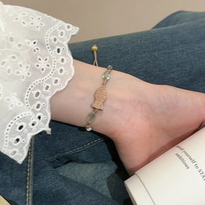 Detail eines Perlenarmbands mit Holzfisch-Anhänger und grünen Perlen am Handgelenk