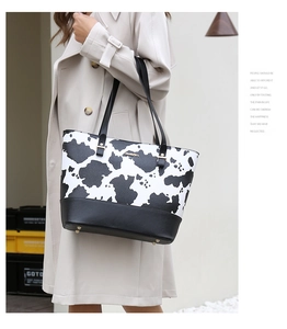 Detail of a cow print tote bag with black faux leather base and metallic feet studs