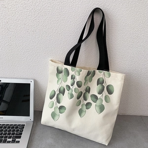 Detail of minimalist cream canvas tote bag with green eucalyptus leaf print and black straps