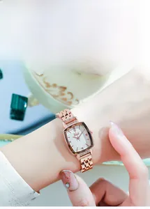 Close-up of a rose gold rectangular watch with crystal accents on a metal chain strap