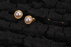 Macro view of minimalist pearl stud earrings with gold frame on charcoal background