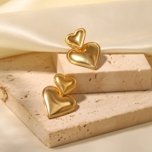 Detail of 18k gold heart-shaped earrings on stone base with satin fabric background