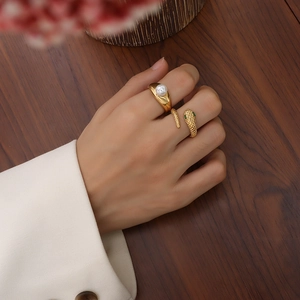 18k gold plated snake-shaped and pearl rings set on female hand with wood background
