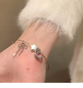 Detail of silver open bangle with pink heart zircon, star and bow charms on wrist