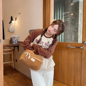 Stylish brown plush cosmetic bag held by a woman in a warm and cozy cafe interior