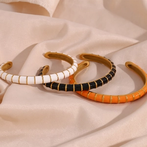 Detail of three colorful enamel C-shape open bangles on cream silk background