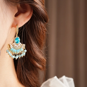 Détail macro de boucles d'oreilles éventail vintage avec zircon bleu et pompons perlés