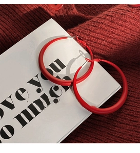 Close-up of matte red acrylic C-shaped hoop earrings on a vintage knit background