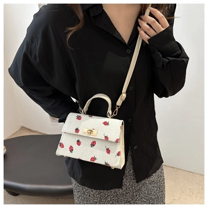 Detail of white corduroy strawberry pattern handbag with golden buckle and beige strap