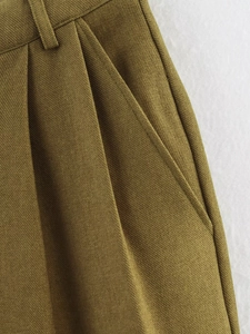 Detailed macro view of olive green twill trousers showing waist pleats and side pocket construction
