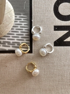 Macro detail of gold and silver pearl hoop earrings on beige linen texture background