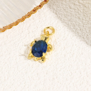 Detail of 18k gold turtle pendant with a deep blue oval gemstone on a textured background