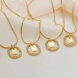 Gold stainless steel oval letter necklace with crystals on white silk background