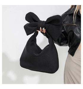Detail of a large black tote bag featuring a prominent decorative bow on the handle