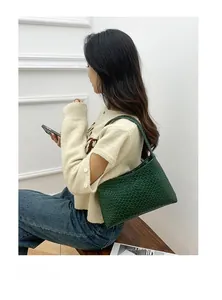 Close-up of deep green woven shoulder bag styled with casual knitwear and blue jeans