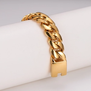 Polished gold stainless steel Cuban link bracelet displayed on a white cylindrical stand