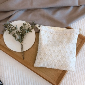 Detailed view of white floral lace drawstring pouch with elegant tassel on a wooden tray