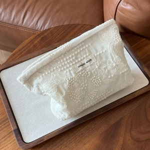 Detail showing vintage white lace embroidery on cotton makeup bag with woven label