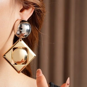 Close-up of geometric gold and silver metal earrings worn by a model in professional lighting