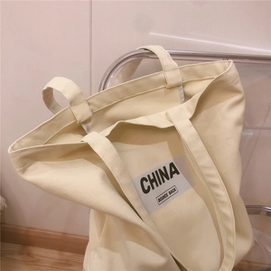 Détail d'un grand sac cabas en toile kaki avec imprimé China accroché sur une chaise