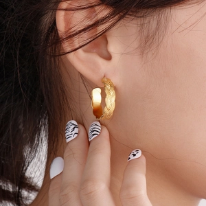 Macro shot of 18k gold plated braided texture hoop earring on model's ear