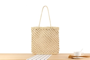 Detail of beige hand-woven tote bag with mesh texture on a light wood surface