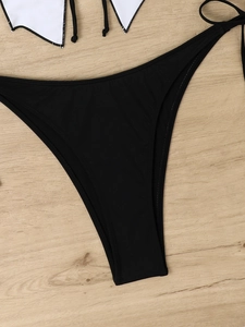 Flat lay of high-cut black bikini bottoms on a light wood background for fashion swimwear