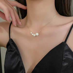Gros plan d'un collier chaîne dorée avec cinq perles blanches dégradées sur le décolleté