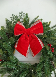 Detail of red velvet Christmas bow with glitter edges on green festive pine needles wreath