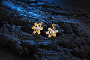 Detailed macro view of gold flower earrings featuring a central white pearl inlay