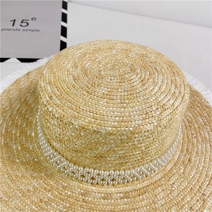 Detail of straw boater hat featuring elegant faux pearl bands and frayed edge texture