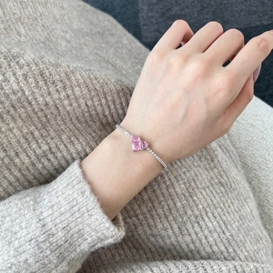 Close-up of S925 silver tennis bracelet with pink heart gemstone on a knit sweater